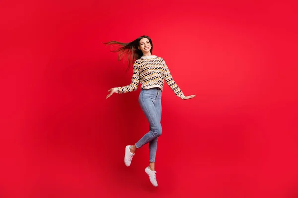 Tamanho do corpo de comprimento total foto de menina alegre pulando com sopro de cabelo isolado vibrante cor vermelha fundo — Fotografia de Stock
