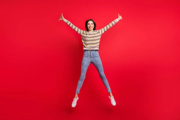 Tamanho do corpo de comprimento total foto de menina feliz em suéter saltando alto como estrela alegre isolado cor vermelha brilhante fundo — Fotografia de Stock