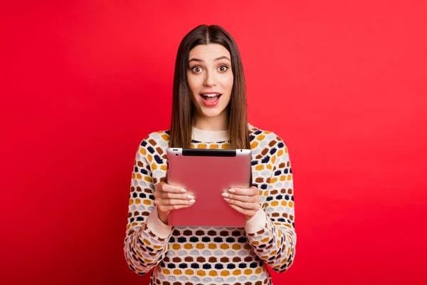 印象的な女の子の肖像画は、赤い色の背景に隔離されたカラフルなセーターを着てタブレットを保持 — ストック写真
