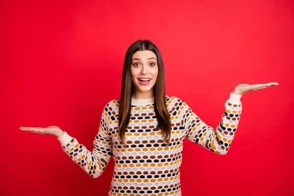 Retrato de chica agradable impresionado mantener espacio vacío desgaste suéter colorido aislado sobre fondo de color rojo — Foto de Stock