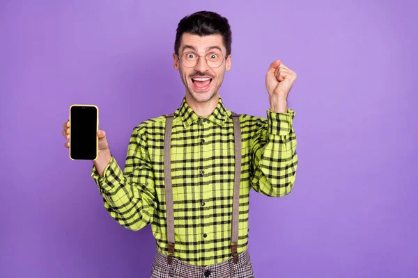 Foto de jovem feliz animado sorrindo homem positivo mostrar telefone segurar punho na vitória isolado no fundo cor violeta — Fotografia de Stock
