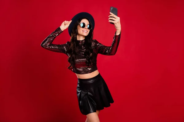 Zdjęcie pani trzymać telefon strzelać selfie nosić błyszczący top kapelusz skóra krótka spódnica specs izolowane czerwony kolor tło — Zdjęcie stockowe