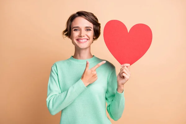 Foto de jovem atraente mulher positiva sorriso ponto dedo papel coração anúncio promo recomendo isolado sobre fundo cor bege — Fotografia de Stock