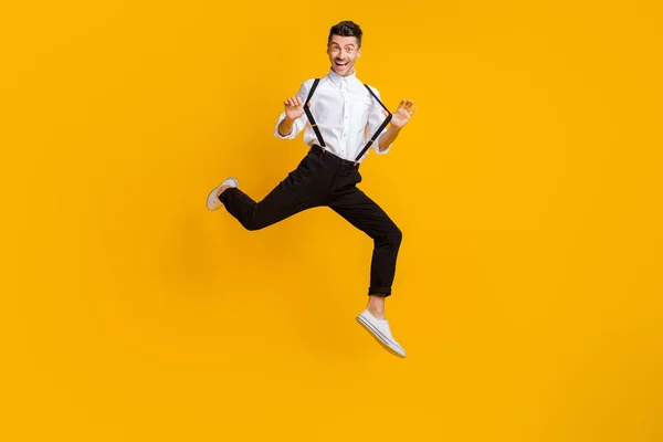 Ganzkörperfoto von fröhlichen Menschen Hände spielen mit Hosenträgern springen hoch isoliert auf gelbem Hintergrund — Stockfoto