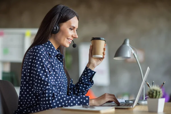 Profile side photo of charming woman hold takeout coffee cup work laptop call center wear headset mic indoors in office