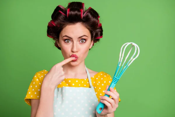 Foto di bella carino ragazza rullo hairdo labbra leccare dito degustazione pasta cuocere biscotto tenere plastica frusta fissando scioccato usura punteggiato grembiule camicia isolato colore verde sfondo — Foto Stock