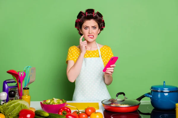 Portrait of her she nice attractive confused nervous funky housewife cooking fresh meal dish find recipe biting lip blogging isolated over green pastel color background