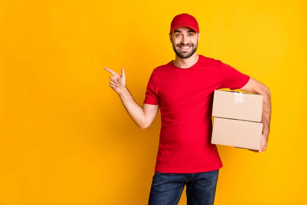 Foto di carino ragazzo corriere vestito vestiti rossi consegna scatola marrone indicando spazio vuoto isolato colore giallo sfondo — Foto Stock