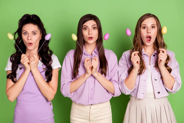 Foto de três meninas surpreendido chocado notícias surpresa segurar ovos paus Páscoa feriado isolado sobre fundo de cor verde — Fotografia de Stock