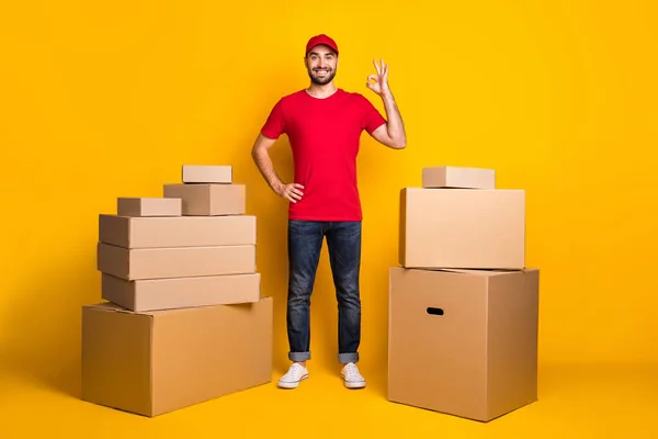 Full length body size photo happy courier with carton boxes showing okay gestured fingers isolated on vivid yellow color background — Foto Stock