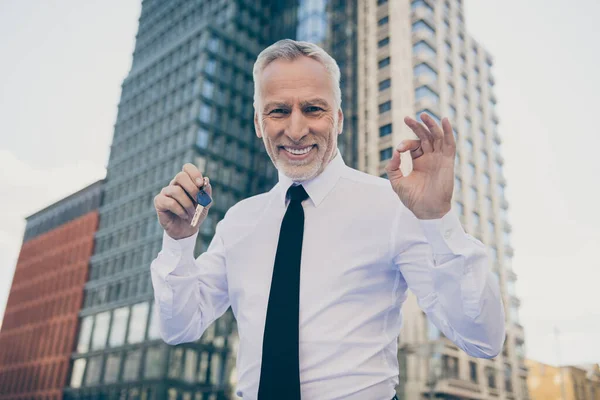 Photo of optimistic old business man hold key show okey sign wear white shirt outdoors near work center — Foto Stock