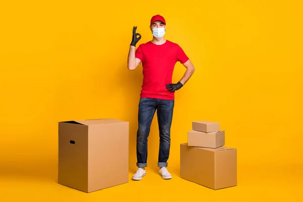 Full length body size view of healthy guy mailman delivering orders wear mask show ok-sign social distance isolated on vivid yellow color background — Foto Stock