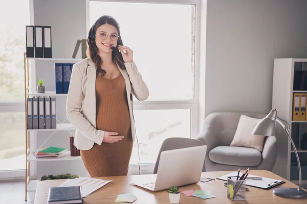 Foto portrét těhotné ženy usmívající se přes sluchátka dotýkající se břicha v moderní kanceláři — Stock fotografie
