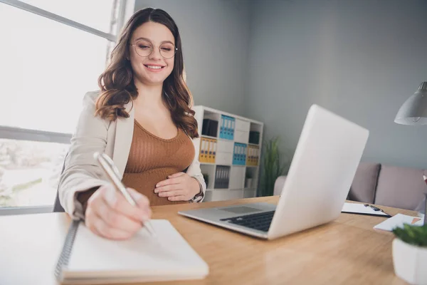 Fotografie těhotné podnikatelky sedící stůl psát poznámkový blok oblek hnědé košile pracovní stanice kancelář vnitřní — Stock fotografie