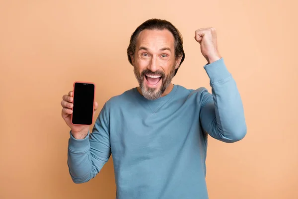 Foto retrato de homem de meia-idade mostrando tela do smartphone copyspace gesticulando como vencedor isolado no fundo de cor bege pastel — Fotografia de Stock