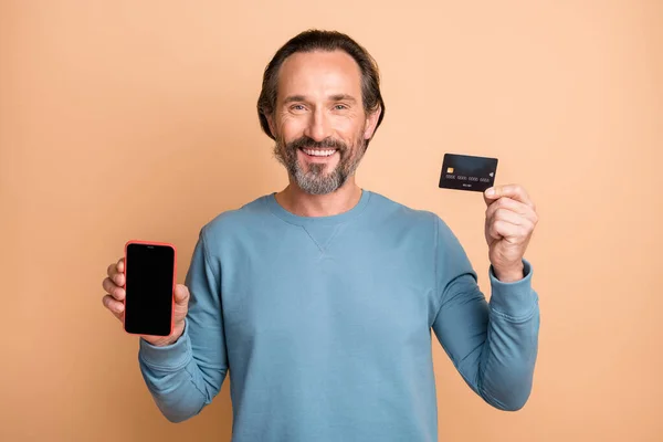Foto retrato de segurando telefone com cartão de crédito espaço em branco isolado no fundo de cor bege pastel — Fotografia de Stock