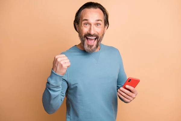 Foto retrato de homem feliz mantendo o smartphone gesticulando como vencedor gritando isolado no fundo de cor bege pastel — Fotografia de Stock