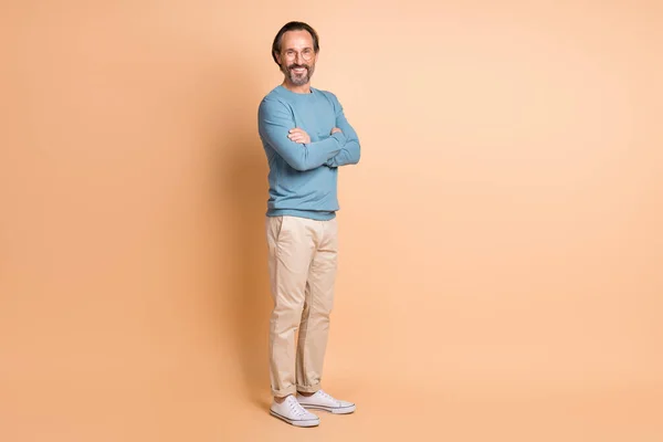 Full length photo of man folded arms wear glasses blue sweater pants sneakers isolated beige color background