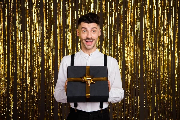 Photo of cute impressed young guy dressed glamour outfit getting black gift box isolated shiny golden background