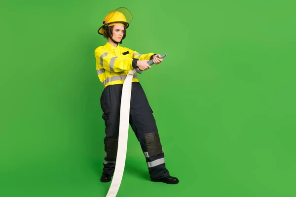 Πλήρης φωτογραφία μήκος του σοβαρού γοητευτικό νεαρή πυροσβέστης ντυμένος κίτρινο ομοιόμορφη εκμετάλλευση σωλήνα κενό χώρο απομονωμένο πράσινο φόντο χρώμα — Φωτογραφία Αρχείου