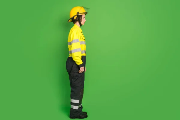 Фотографія повної довжини впевненої красивої пожежної жінки, одягнений жовтий однорідний шолом, виглядає порожнім простором ізольований зелений колір фону — стокове фото
