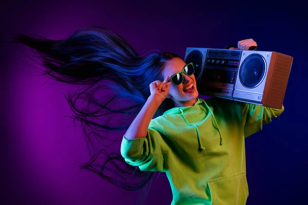 Foto de loca feliz alegre joven mujer usar gafas de sol volar pelo mantenga boombox aislado sobre fondo de neón —  Fotos de Stock