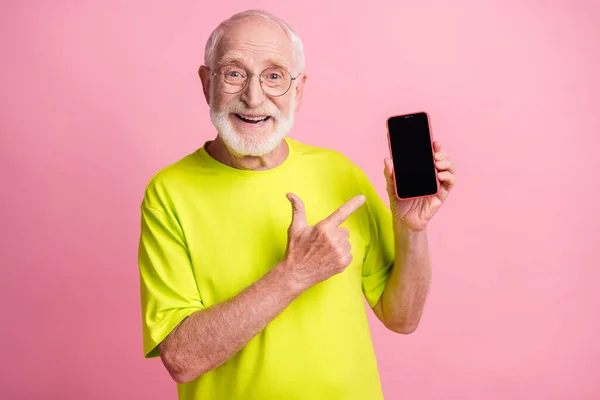 Mutlu, mutlu, gülümseyen büyükbabanın fotoğrafı pembe arka planda izole edilmiş bir cep telefonuna limon tişörtü parmağıyla işaret ediyor. — Stok fotoğraf