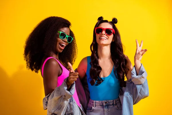 Foto van twee dames directe vinger je v-teken dragen zonneglas jeans outfit geïsoleerde gele kleur achtergrond — Stockfoto