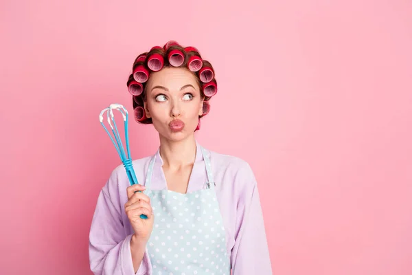 Foto di casa premurosa moglie indossare punteggiato blu grembiule rosso rulli tenendo frusta cercando spazio vuoto isolato colore rosa sfondo — Foto Stock