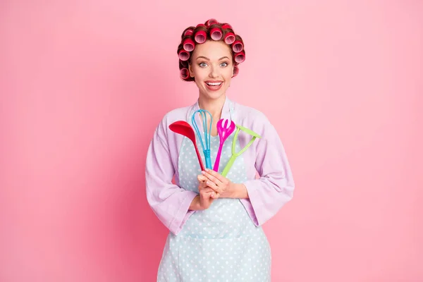 Foto de muito feliz marrom cabelo dona de casa segurar utensílios jantar chef desgaste avental pontilhado isolado no fundo cor-de-rosa — Fotografia de Stock