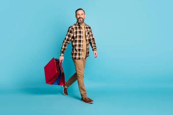 Full size foto van volwassen positieve man gaan winkelen hold tassen pakketten geïsoleerd over blauwe kleur achtergrond — Stockfoto