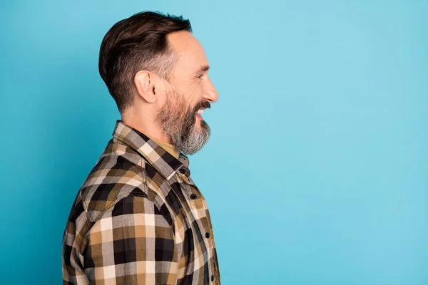 Foto de perfil lateral retrato del hombre sonriendo buscando espacio vacío en camisa a cuadros aislado sobre fondo de color azul brillante —  Fotos de Stock