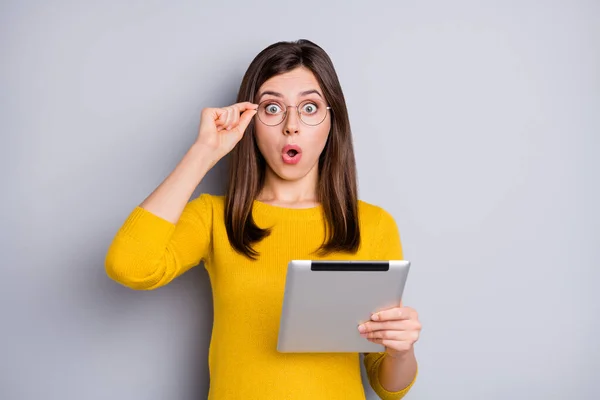 Retrato de la encantadora chica sorprendida sosteniéndose en las manos usando los labios de la tableta hojear noticias aisladas sobre fondo de color gris — Foto de Stock