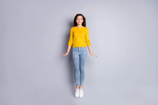 Full size photo of optimistic brunette nice lady jump wear yellow sweater jeans sneakers isolated on grey color background — Stock Photo, Image