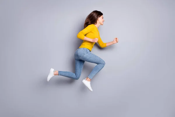 Foto de perfil em tamanho completo de otimista morena agradável salto correr desgaste camisola amarela jeans tênis isolado no fundo de cor cinza — Fotografia de Stock