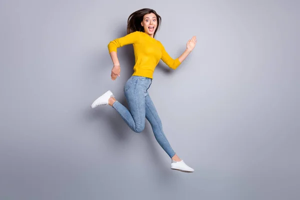 Full storlek profil foto av hurra brunett trevlig dam hoppa springa bära tröja jeans sneakers isolerad på grå färg bakgrund — Stockfoto