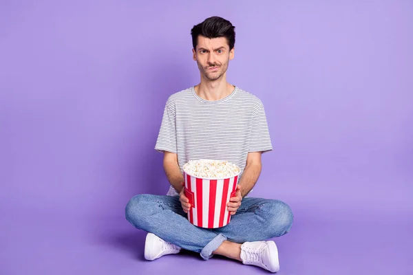 Foto di ragazzo tenere popcorn secchio scontento usura strisce nero t-shirt jeans calzature isolato sfondo viola — Foto Stock