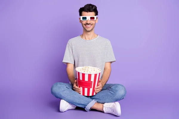 照片上的男人拿着爆米花桶穿着3D斑点白色T恤牛仔裤运动鞋孤立的紫色背景 — 图库照片