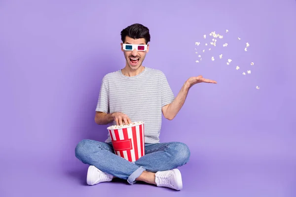 Фото сумасшедшего парня держать коробку бросить попкорн открытым ртом носить 3D очки футболки джинсы кроссовки изолированный фиолетовый фон — стоковое фото