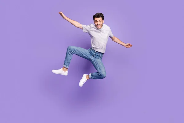 Foto von funky crazy guy springen heben Hände Flugzeug Pose tragen gestreifte T-Shirt Jeans Turnschuhe isoliert lila Hintergrund — Stockfoto