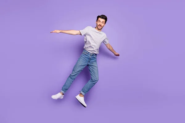 Zdjęcie zszokowany facet skakać samolot pozować nosić biały t-shirt dżinsy obuwie izolowane fioletowe tło — Zdjęcie stockowe