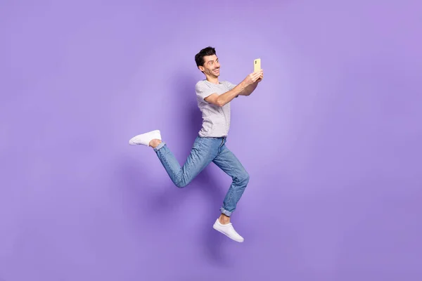 Bild av killen hoppa håll telefon SMS bära vit t-shirt jeans skor isolerad lila bakgrund — Stockfoto