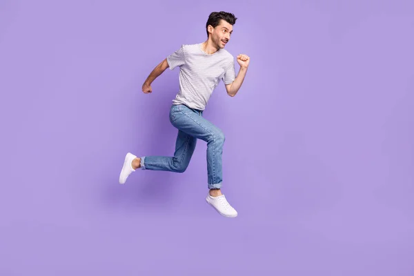 Profil zdjęcie facet skok bieg wygląd pusty przestrzeń nosić czarny t-shirt dżinsy obuwie izolowane fioletowe tło — Zdjęcie stockowe