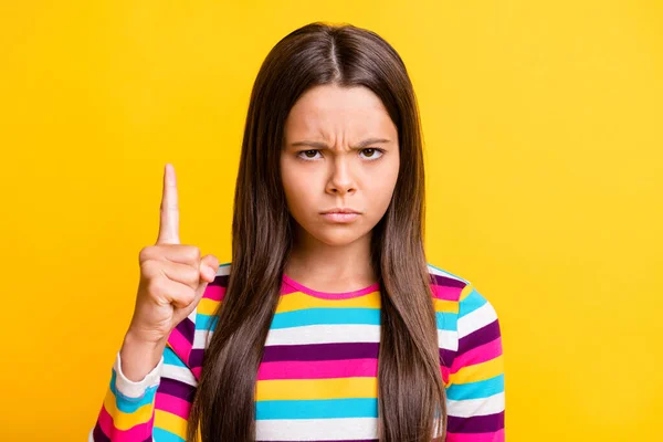 Foto de estricta niña pequeña frunciendo el ceño mirar cámara levantar el dedo directamente hacia arriba usar camisa rayada aislado color amarillo fondo — Foto de Stock