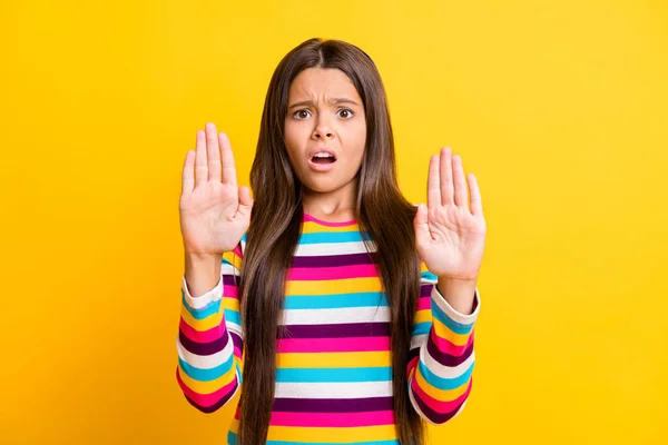 小女孩抬起两只手的照片显示她拒绝穿条纹衬衫孤立的黄色背景 — 图库照片