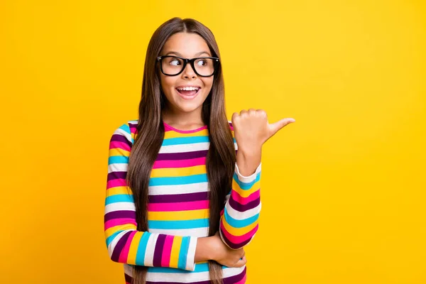 Foto retrato de estudante surpreendida apontando para espaço em branco vestindo listrado jumper sorrindo isolado vibrante cor amarela fundo — Fotografia de Stock