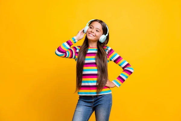 Portret dziewczynki uśmiechniętej szczęśliwie dotykającej słuchawek słuchającej muzyki odizolowanej na jaskrawym żółtym tle — Zdjęcie stockowe