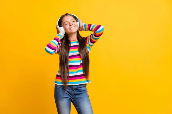 Foto retrato de menina sorrindo tocando fones de ouvido ouvindo música com olhos fechados isolados no fundo de cor amarelo brilhante — Fotografia de Stock
