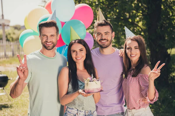 Foto de estudantes de cabelos castanhos positivos felizes mostram v-sign tem festa de aniversário desgaste cones segurar bolo fora no quintal ao ar livre — Fotografia de Stock