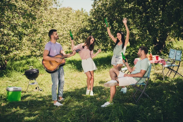 Foto de tamaño completo de cuatro amigos sonrisa alegre celebrar baile fin de semana cantar guitarra beber cerveza al aire libre en el parque — Foto de Stock
